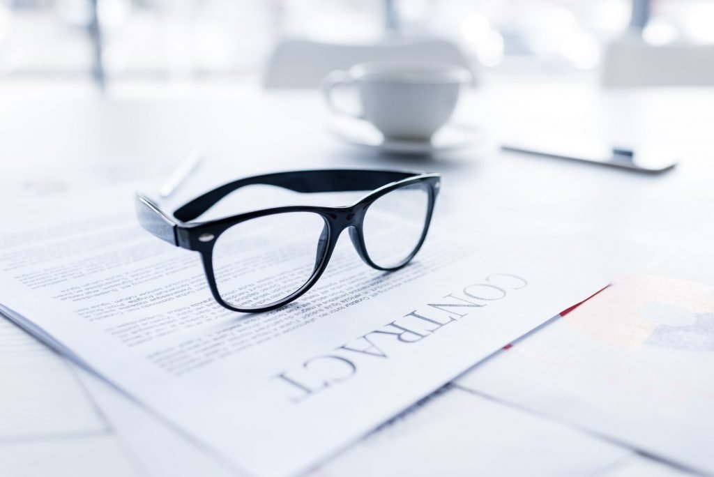 composition with eyeglasses and business contract on white desk