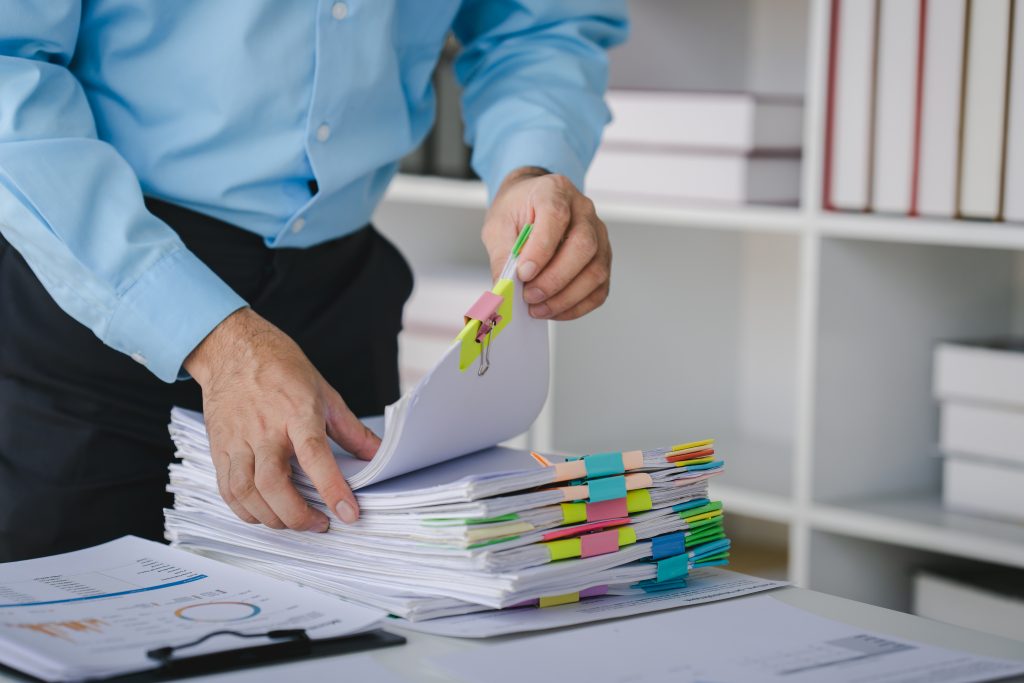 Businessman working on stacks of documents to search for information and check documents on office d