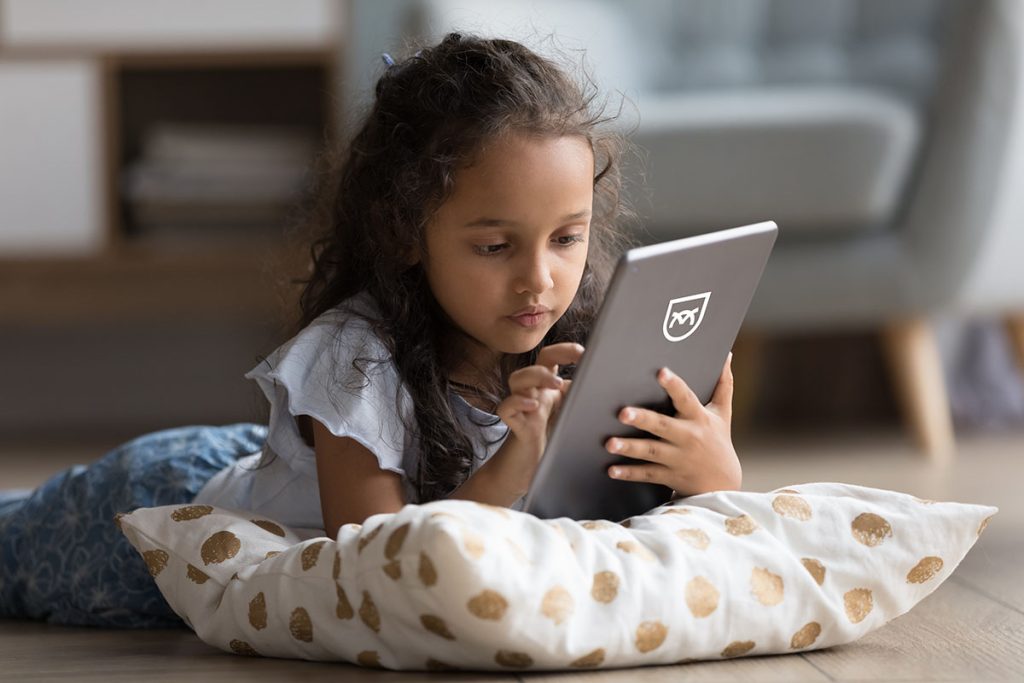 Young girl lying on a pillow and using a tablet device, likely accessing an online app or service, representing the need for COPPA compliance when digital platforms are used by children under 13.
